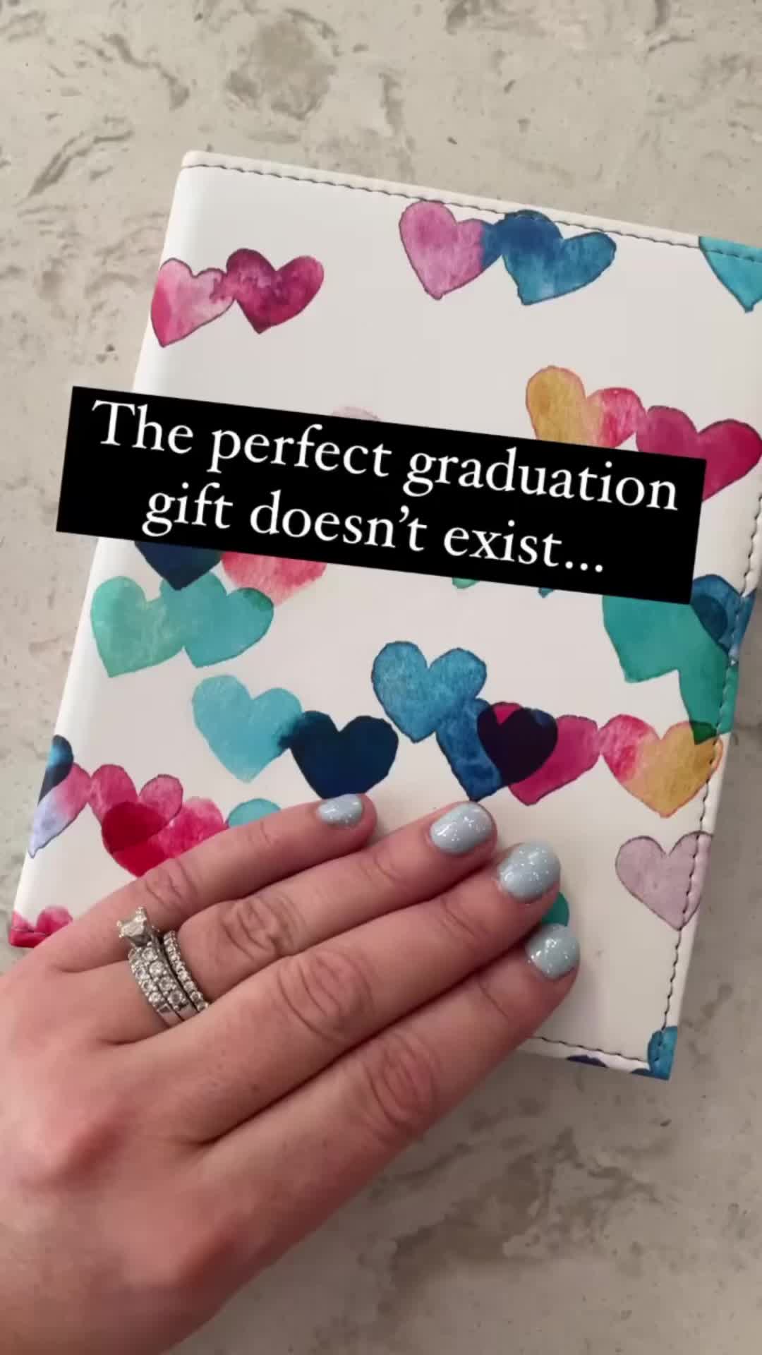 This may contain: a person's hand holding a book with hearts on it and the words, the perfect graduation gift doesn't exist