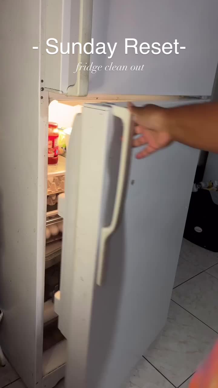 This may contain: a woman reaching into an open refrigerator filled with fruit and vegetables in plastic wrappers