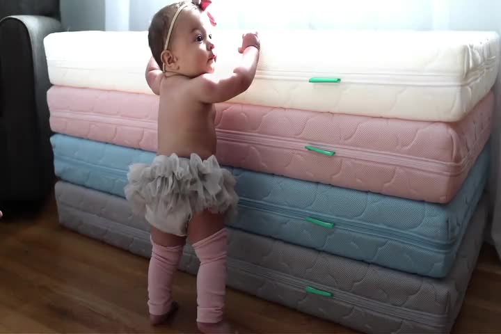 This may contain: a baby girl standing next to several mattresses