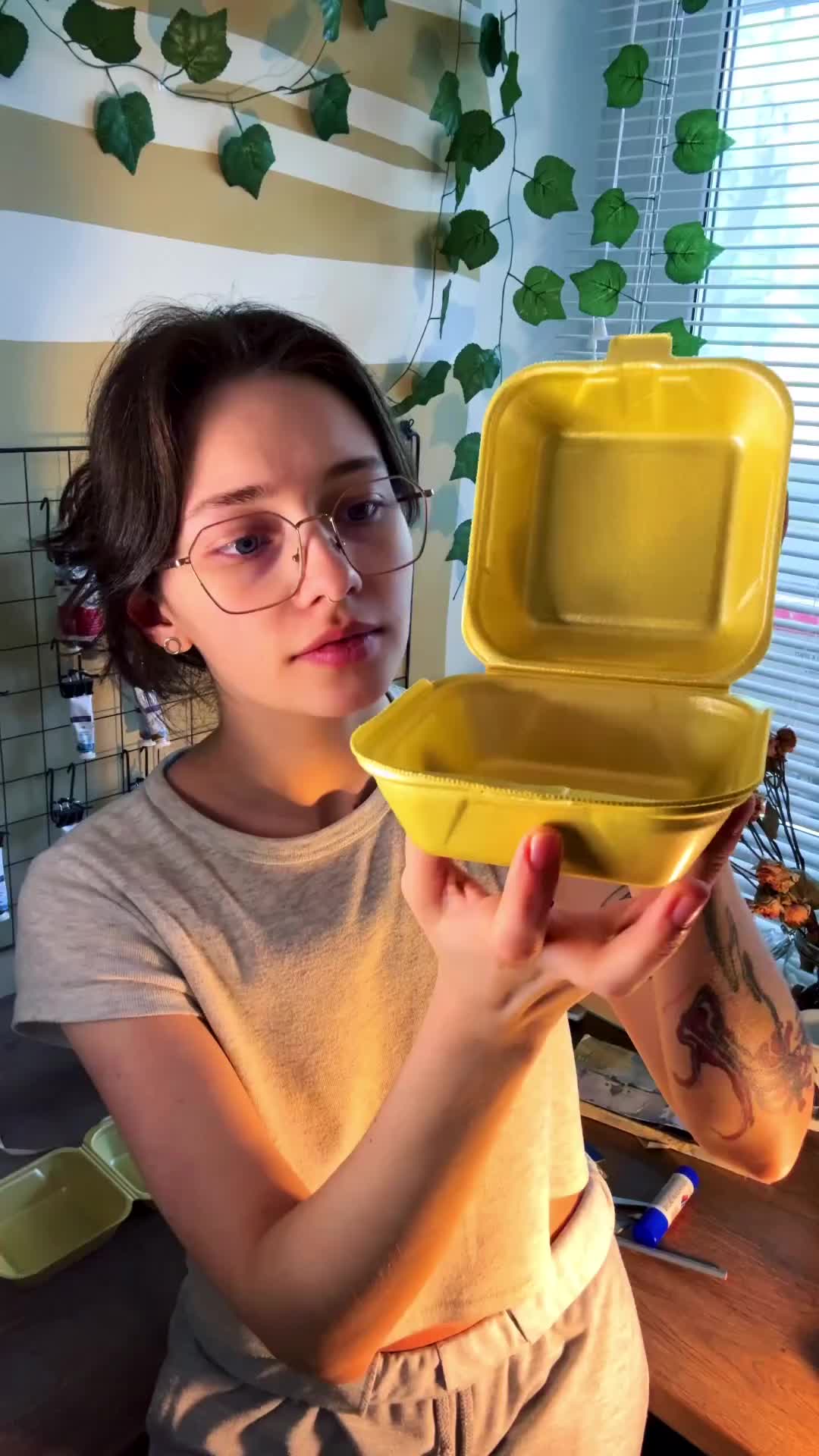 This may contain: a young woman holding up a yellow plastic container in front of her eyeglasses