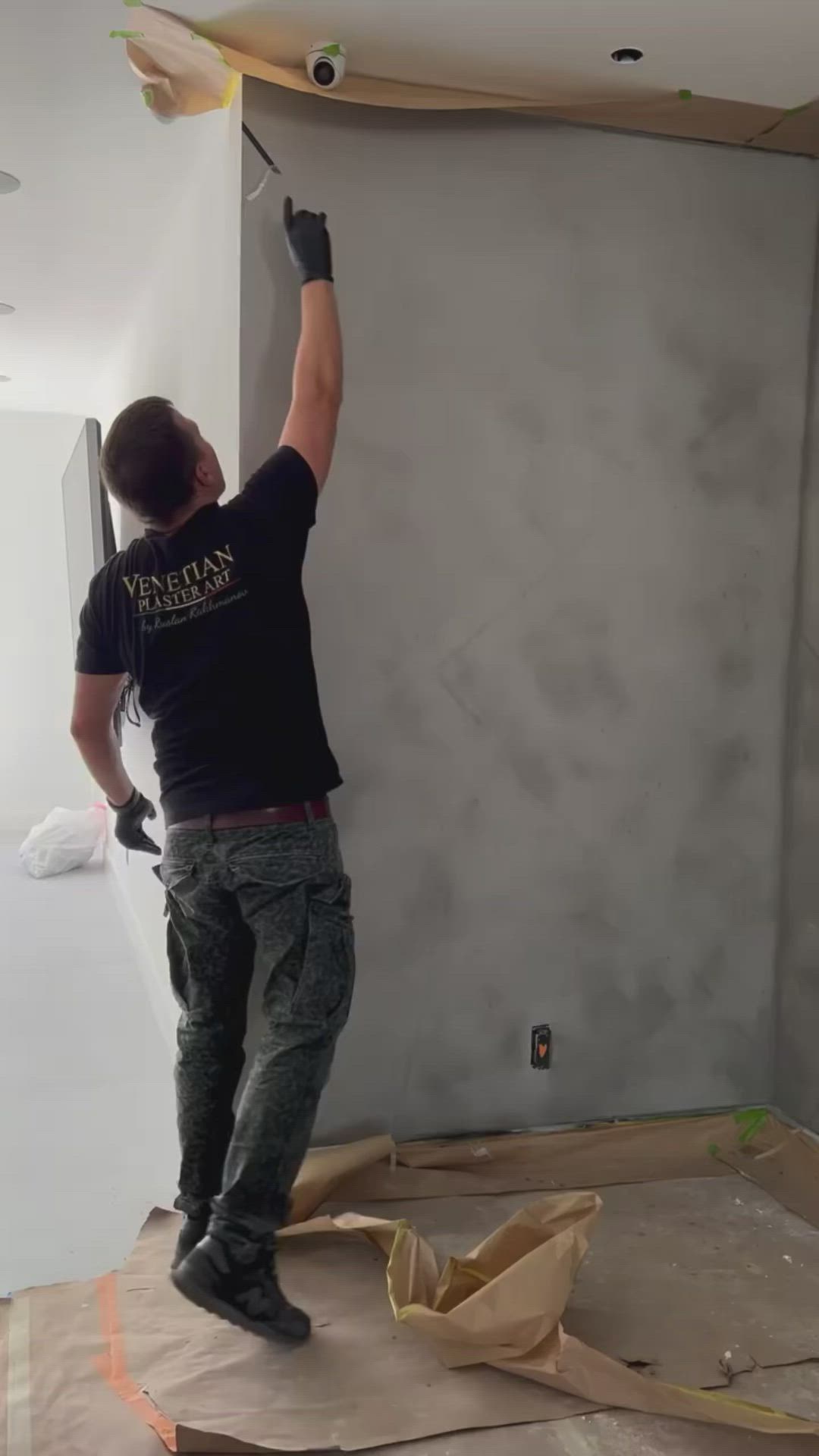 This may contain: a man in black shirt painting a wall with white walls and brown paper on the floor