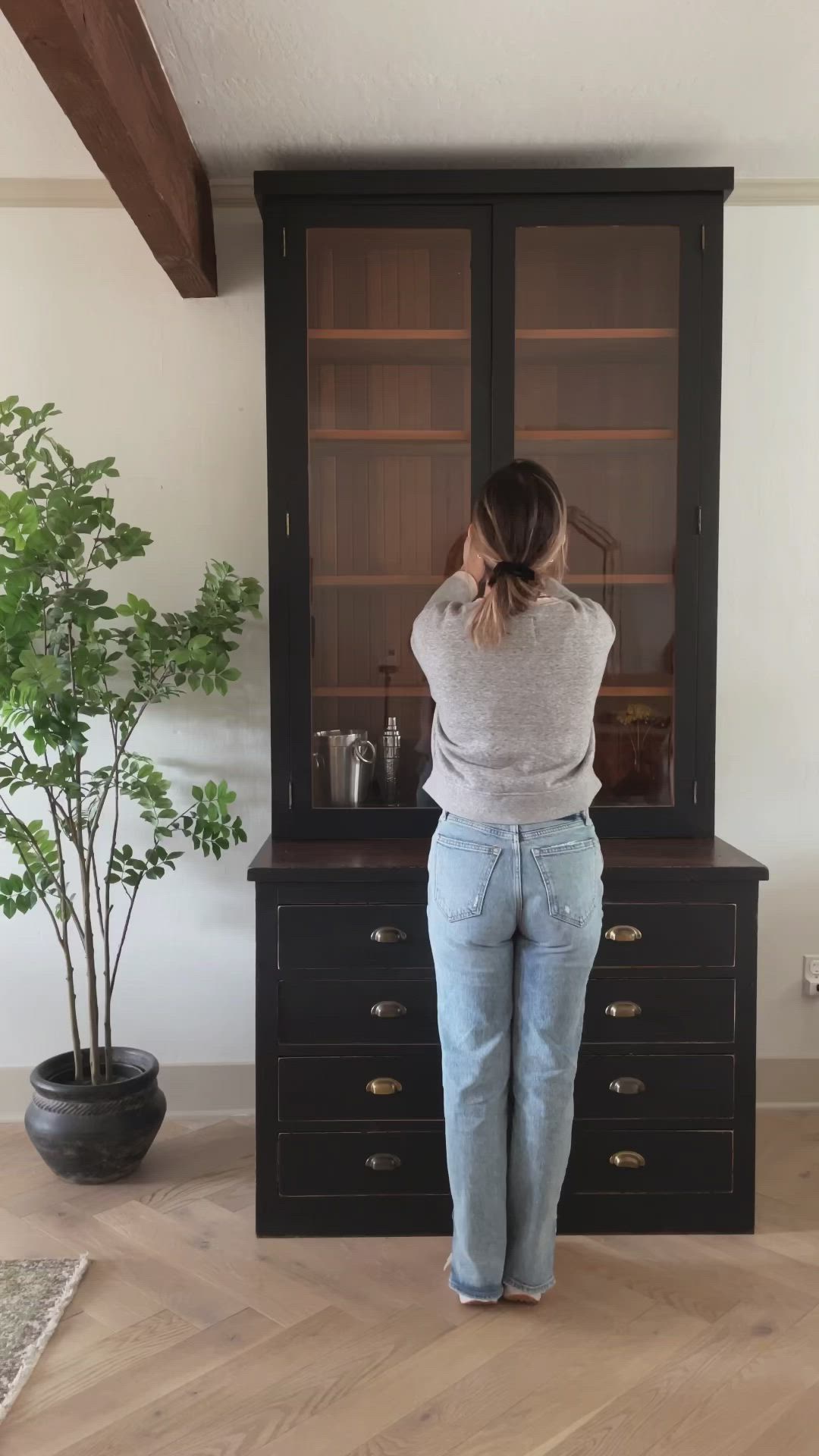 This may contain: a woman standing in front of a black cabinet with glass doors and drawers on it