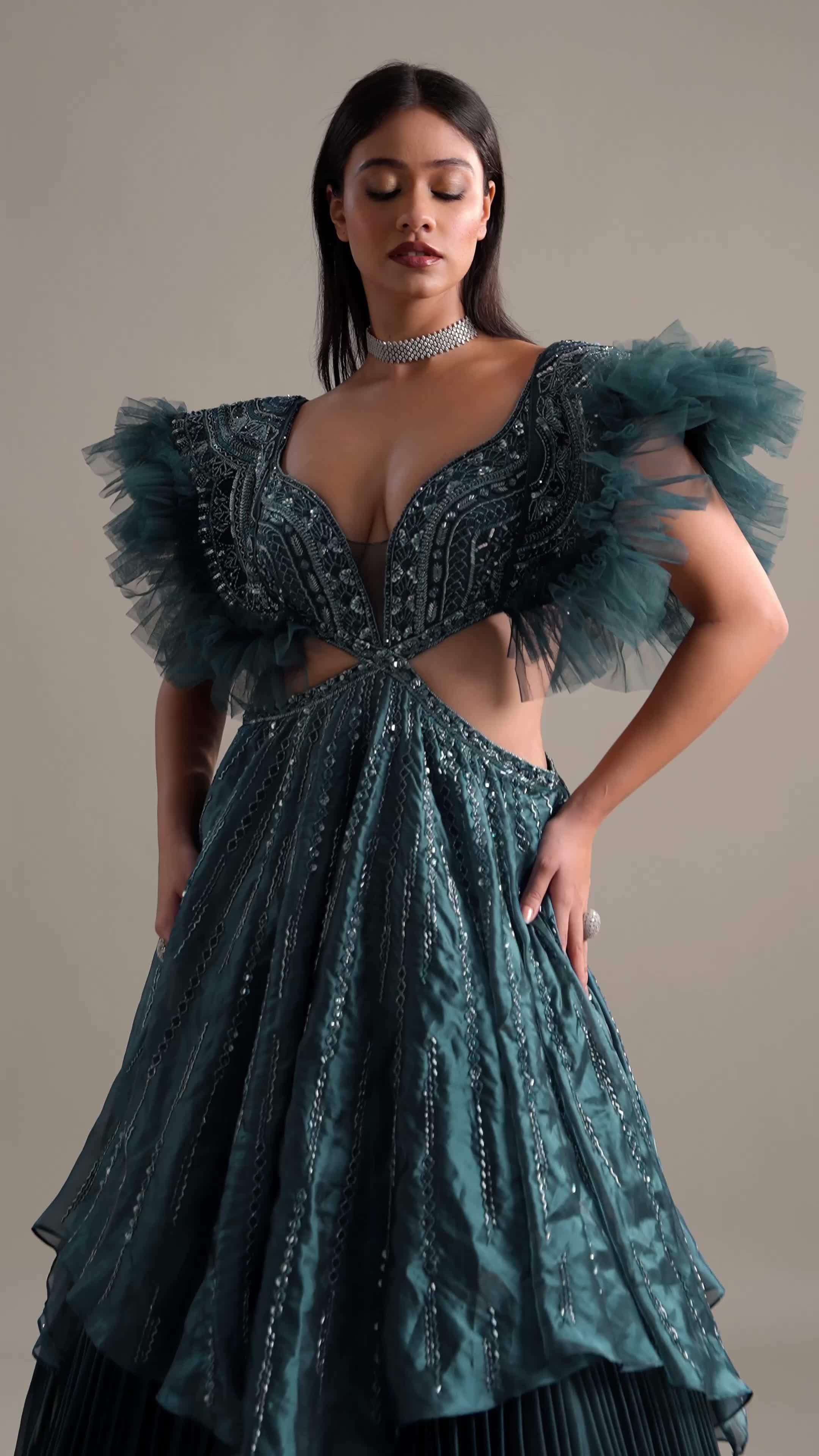 "Experience the height of sophistication with our deep teal blue layered flared gown.

Impeccably crafted from lavish organza, this gown boasts a resplendent double-layered design with a pleated, flared skirt that exudes dramatic flair. 

Adorned with elaborate self-embroidery, it features geometric motifs rendered in cutdana, beads, and other luxurious embellishments. 

