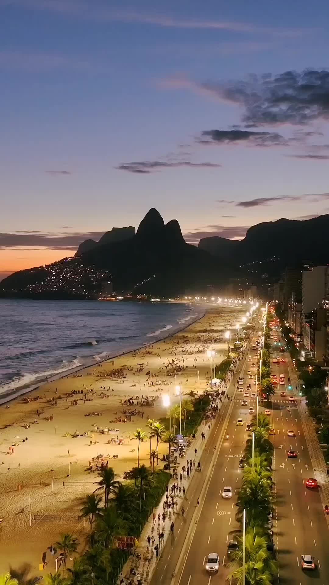 This may contain: an aerial view of the beach and ocean at night with cars parked on the road