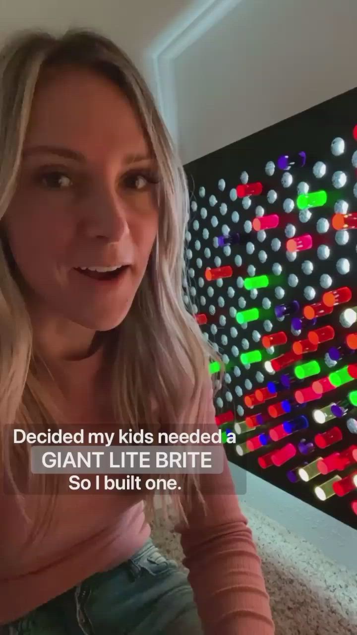 This may contain: a woman is sitting in front of a wall with colorful lights on it and the caption reads, decided my kids needed a giant lite britie so i built one