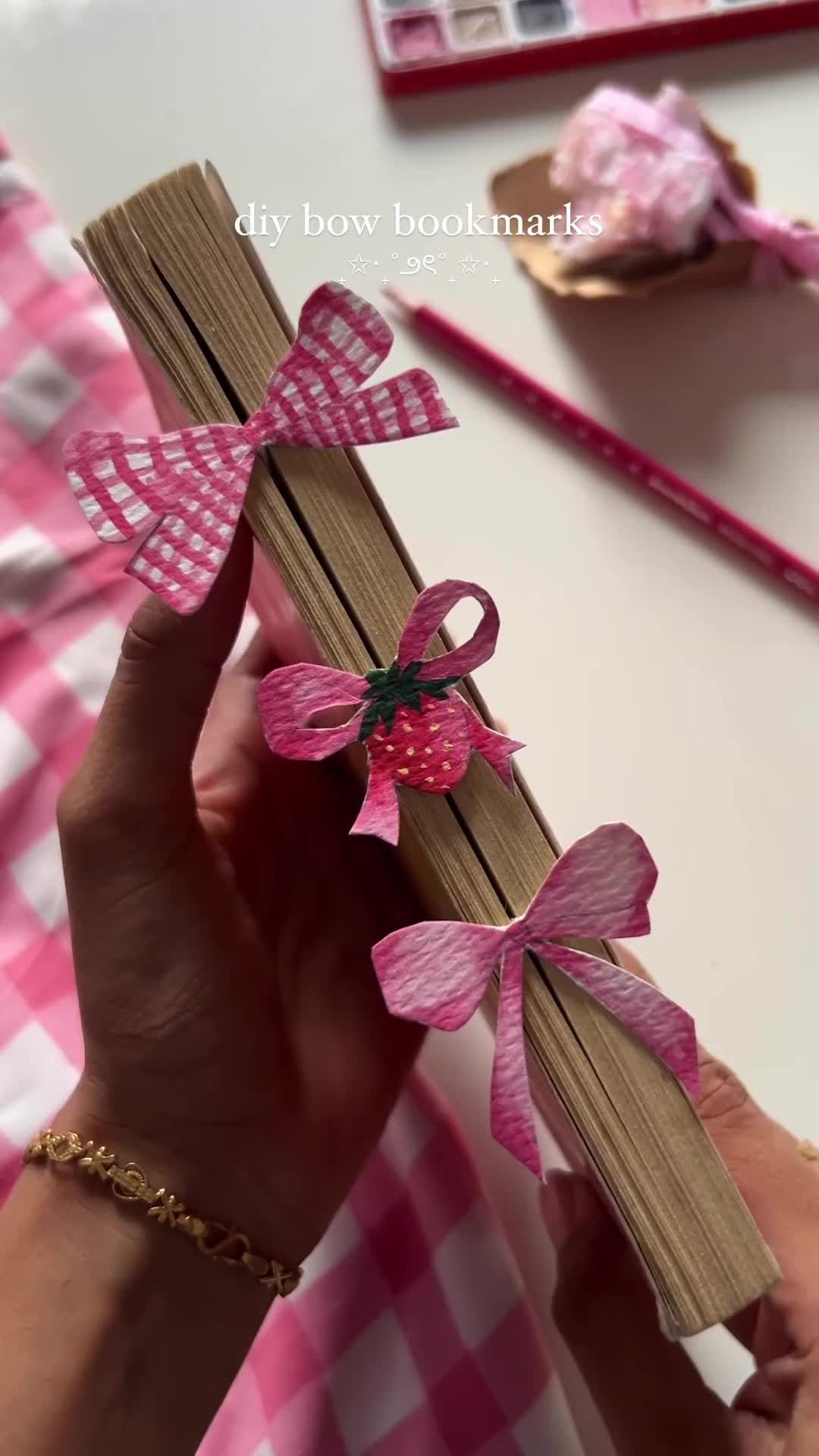 This may contain: a person holding up some pink bows on top of an open wooden book with ribbon