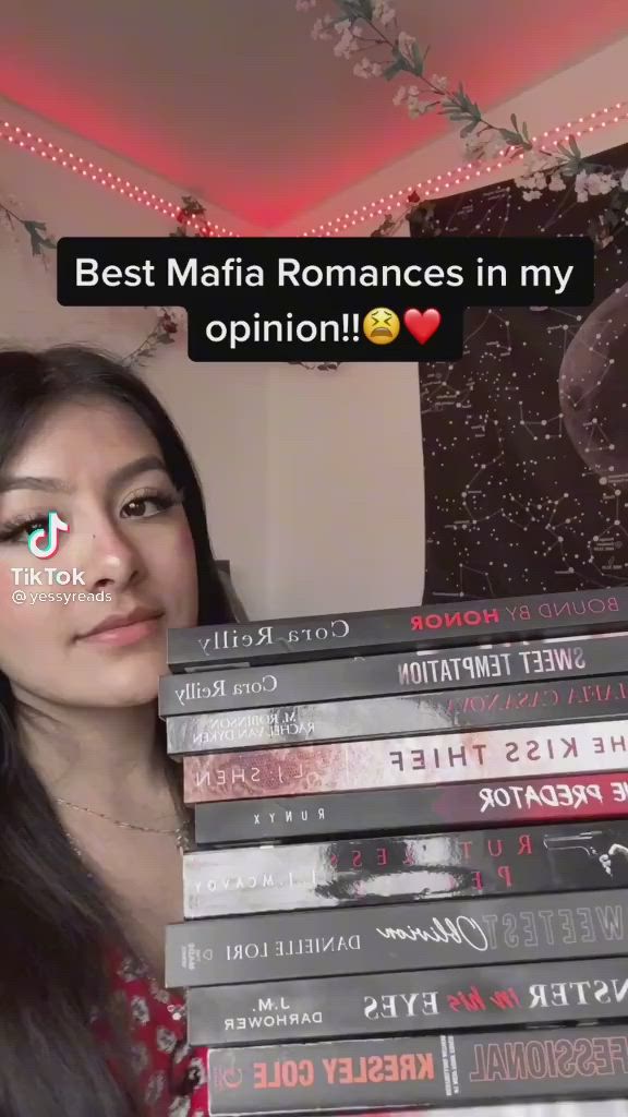 This may contain: a woman holding up a stack of books with the caption best mafia romances in my opinion