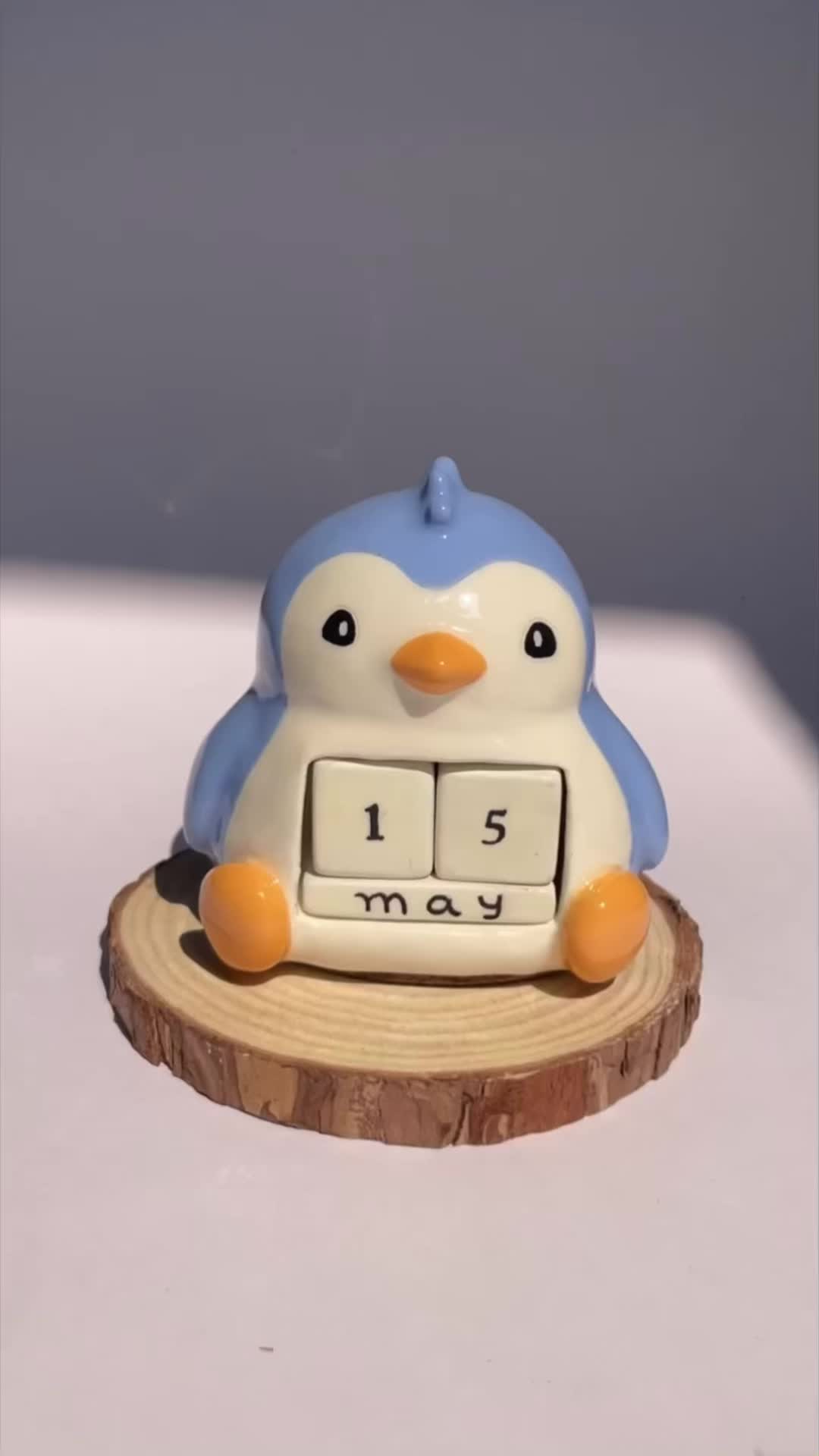 This may contain: a penguin clock sitting on top of a piece of wood