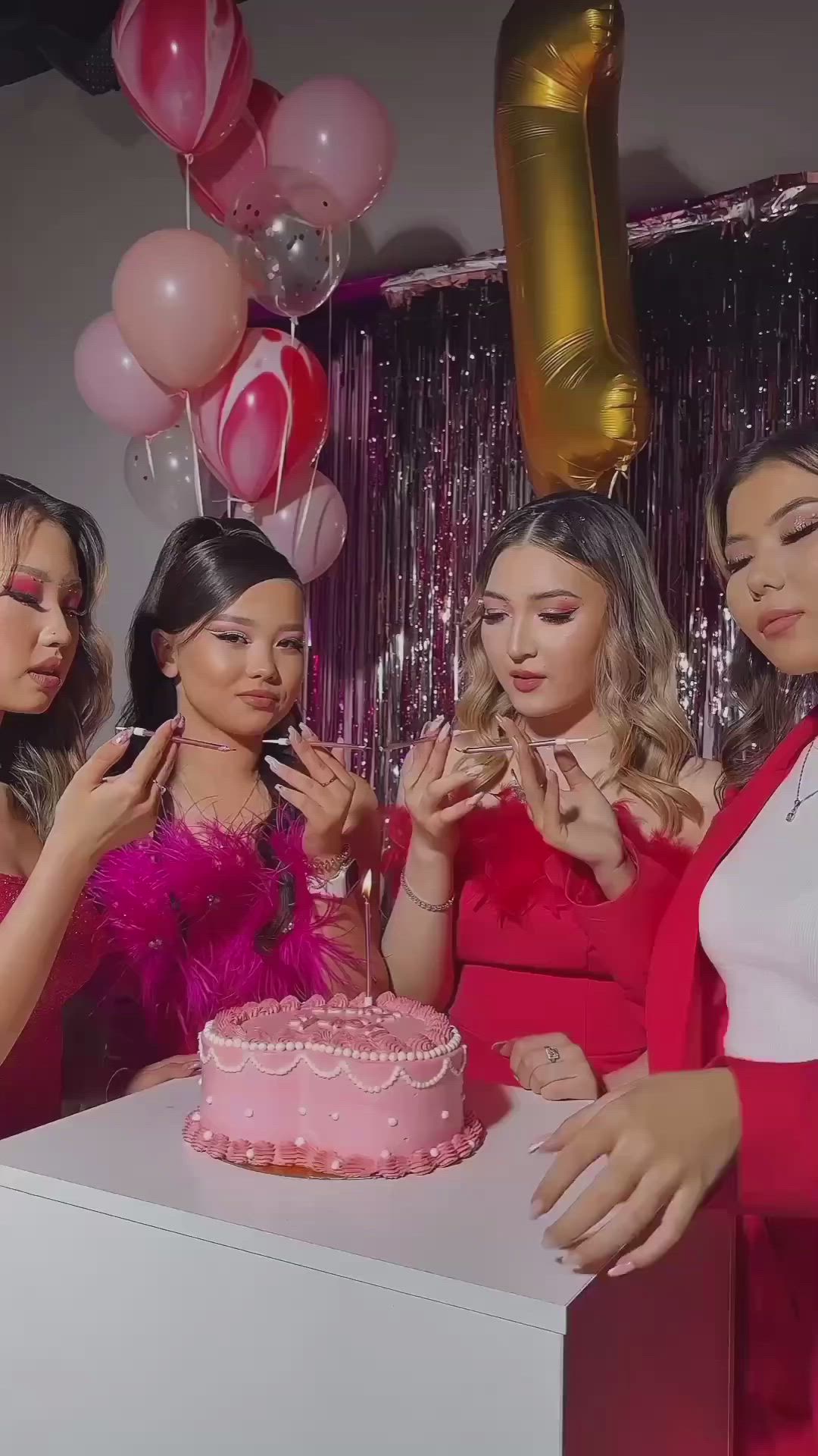 This may contain: three women blowing out candles on a pink cake in front of balloons and streamers