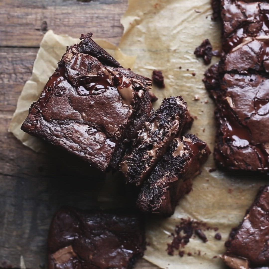 This may contain: chocolate brownies cut into squares and stacked on top of each other next to a piece of parchment paper