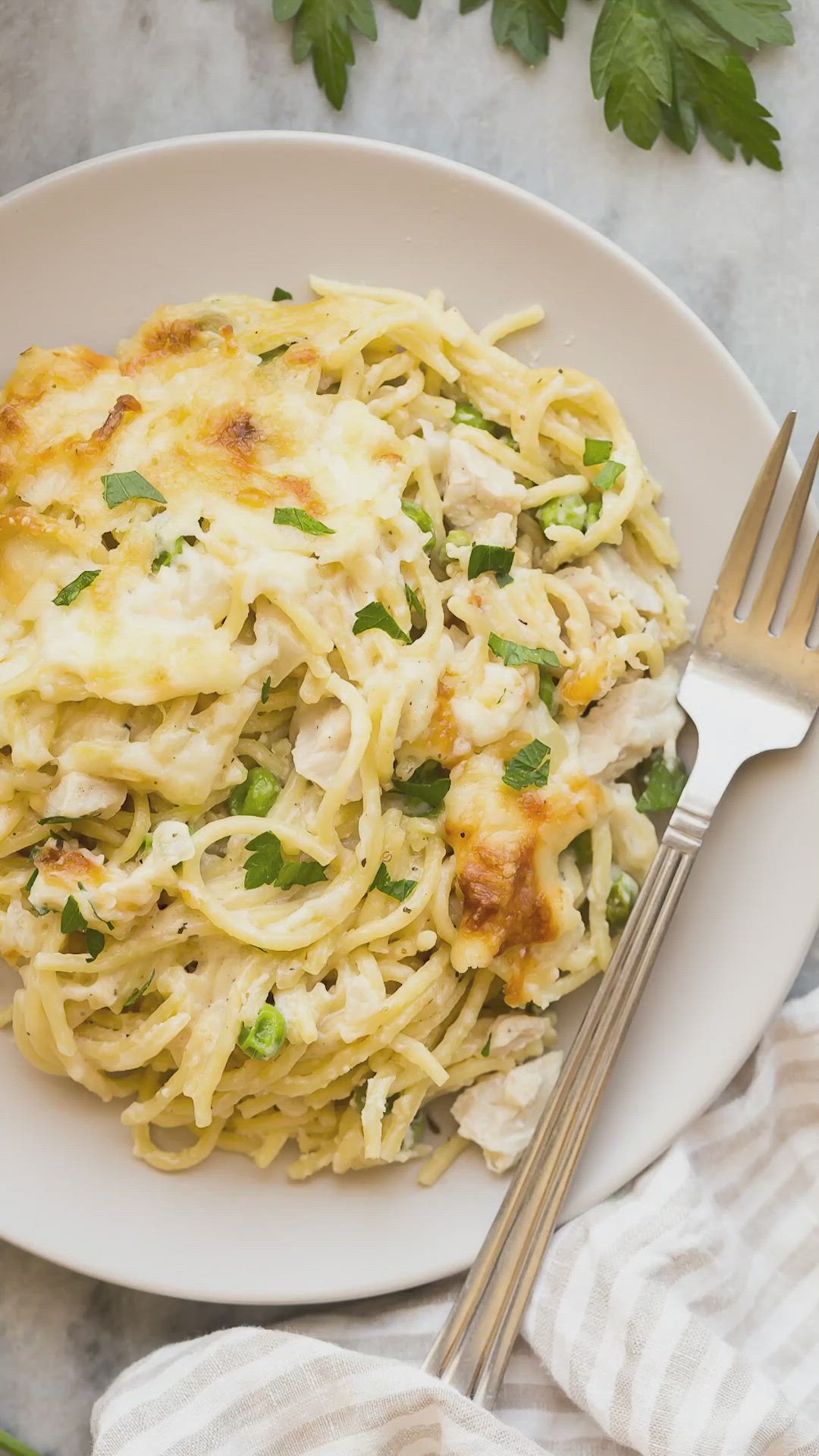 This may contain: a white plate topped with pasta covered in cheese and parsley next to a fork