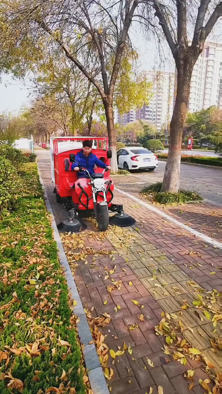 This may contain: a man riding on the back of a red motorcycle down a street next to a tree