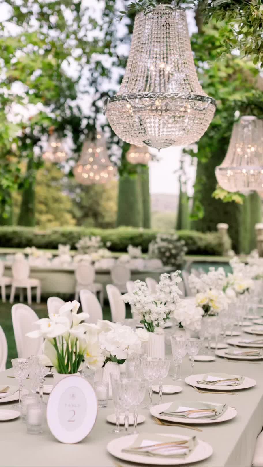 This may contain: a long table with white flowers and chandelier hanging from it's ceiling