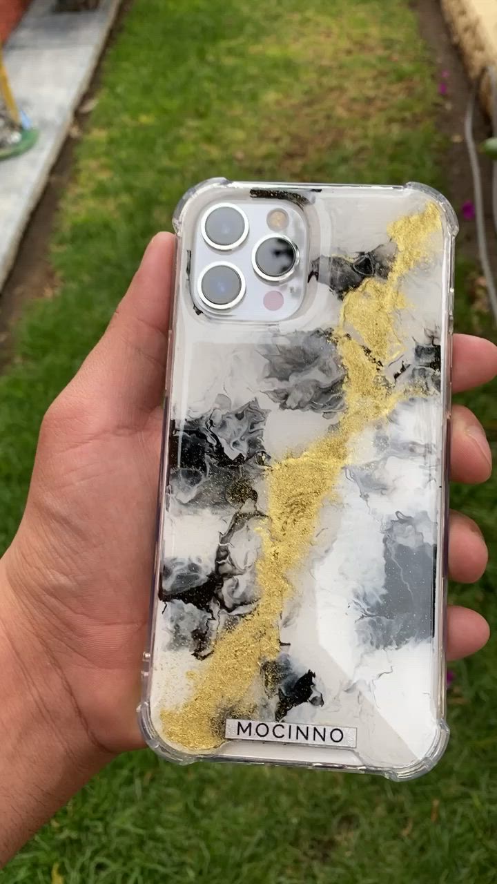 This may contain: a person holding up a phone case with yellow and black paint on it in the grass