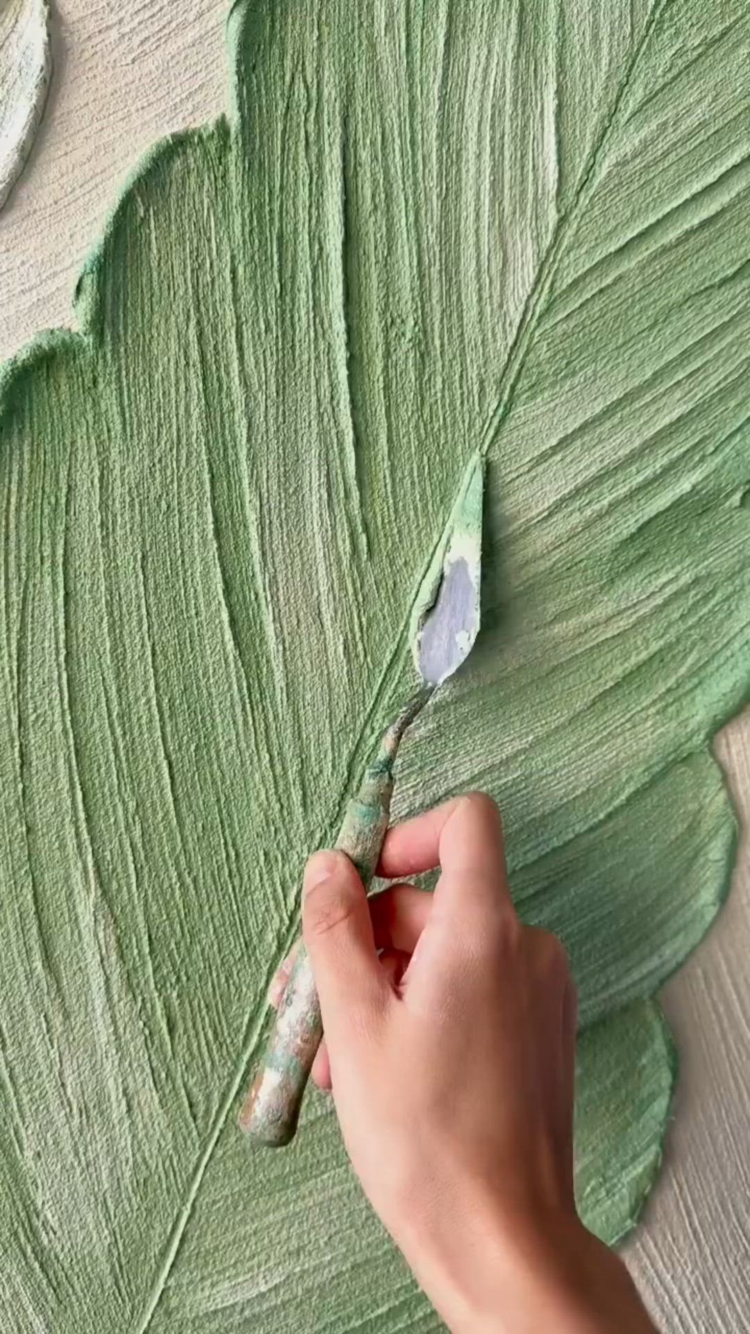 This may contain: someone is painting a large green leaf with white paint on the outside and inside it