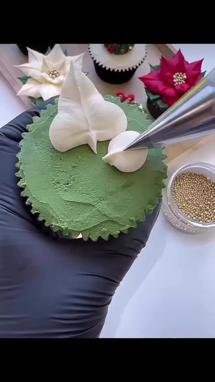 This may contain: a cupcake with green frosting and white flowers on it being cut by a knife