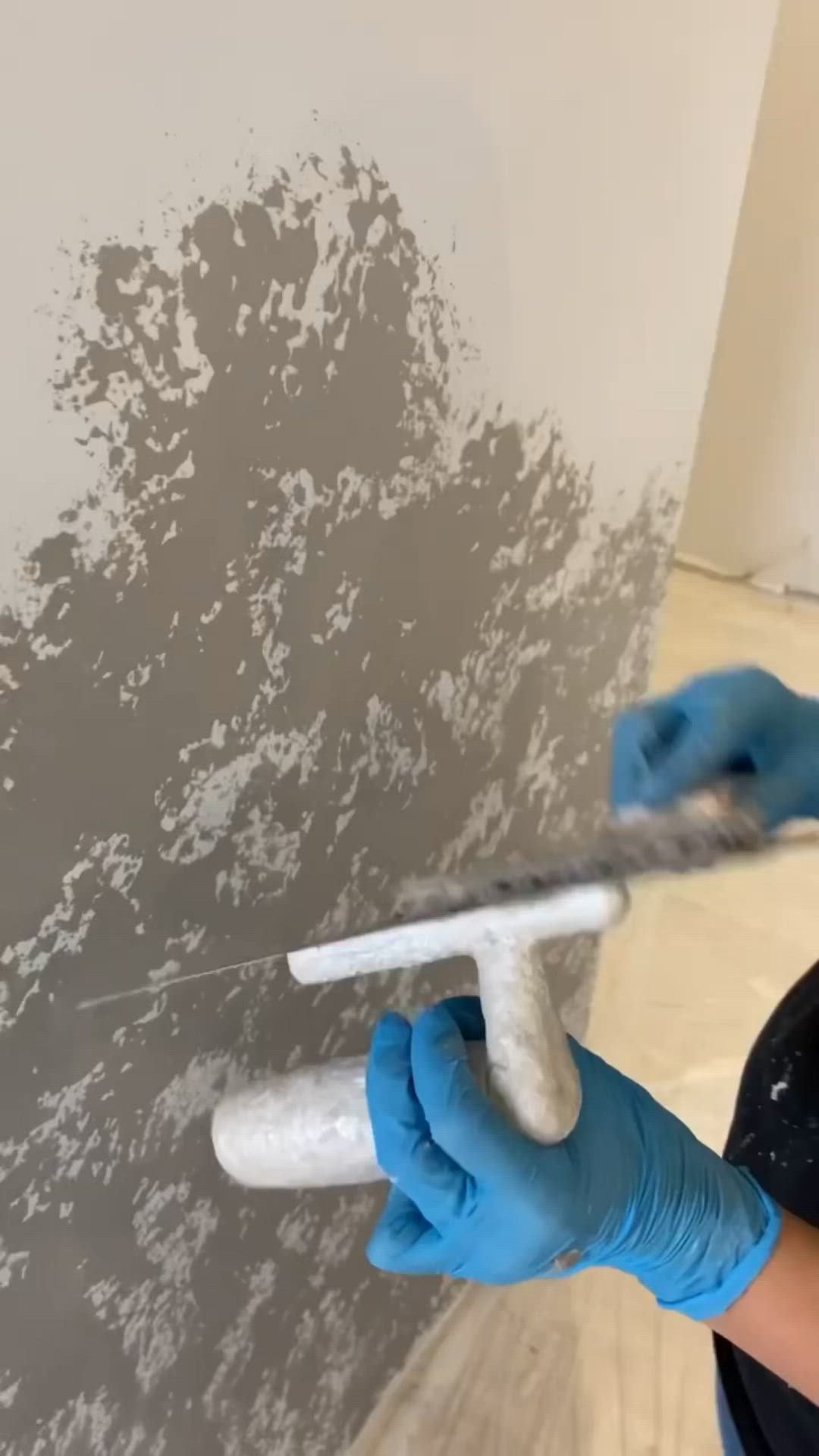 This may contain: a person in blue gloves painting a wall with white paint on the walls and floor