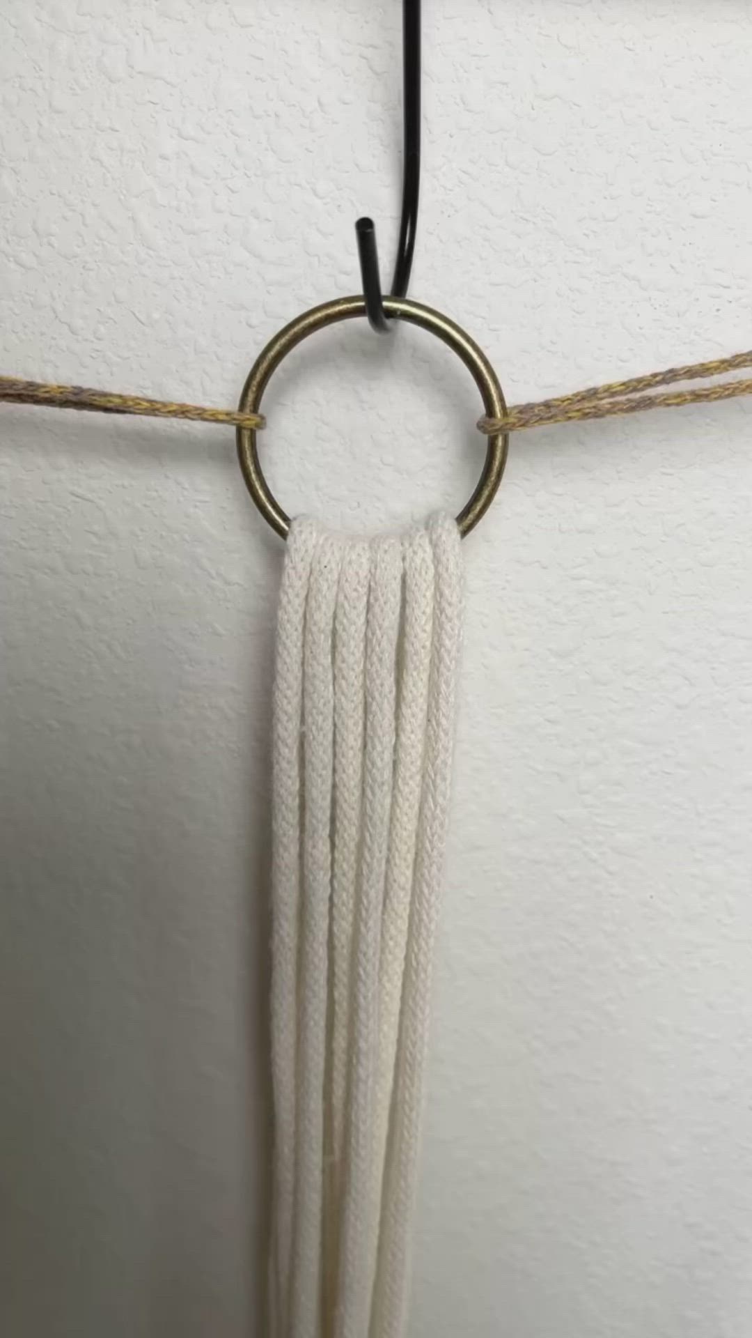 This may contain: a white wall hanging with a metal ring and tassel on it's side