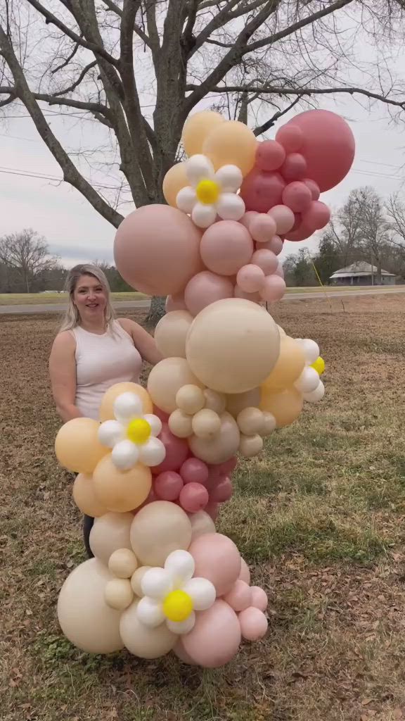 This may contain: a woman standing next to a tall balloon sculpture in the middle of a grass field