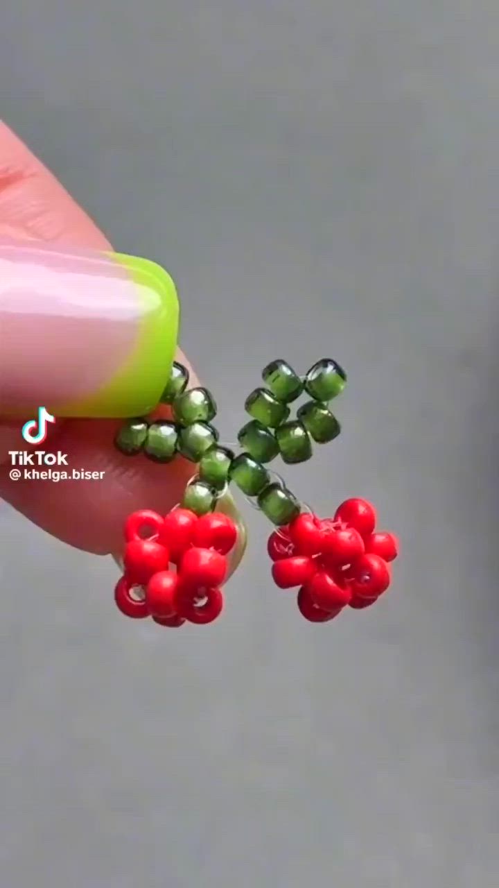 This may contain: someone is holding some tiny red berries on their thumbnails and they are wearing green beads