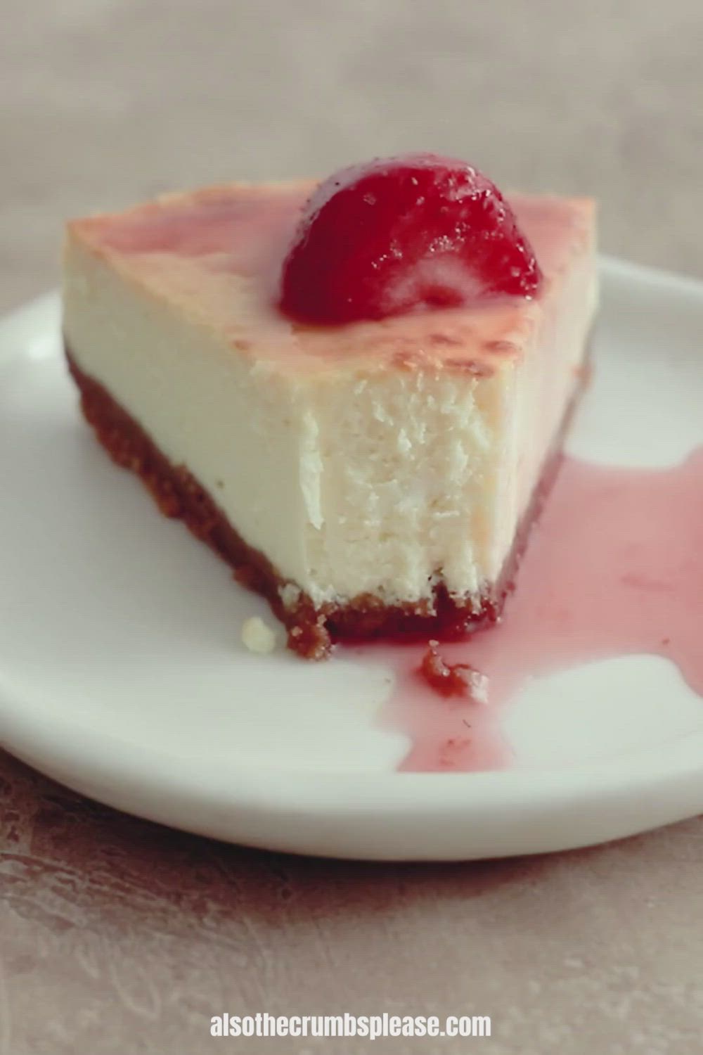 This may contain: a piece of cheesecake on a white plate with a strawberry in the middle and pink glaze