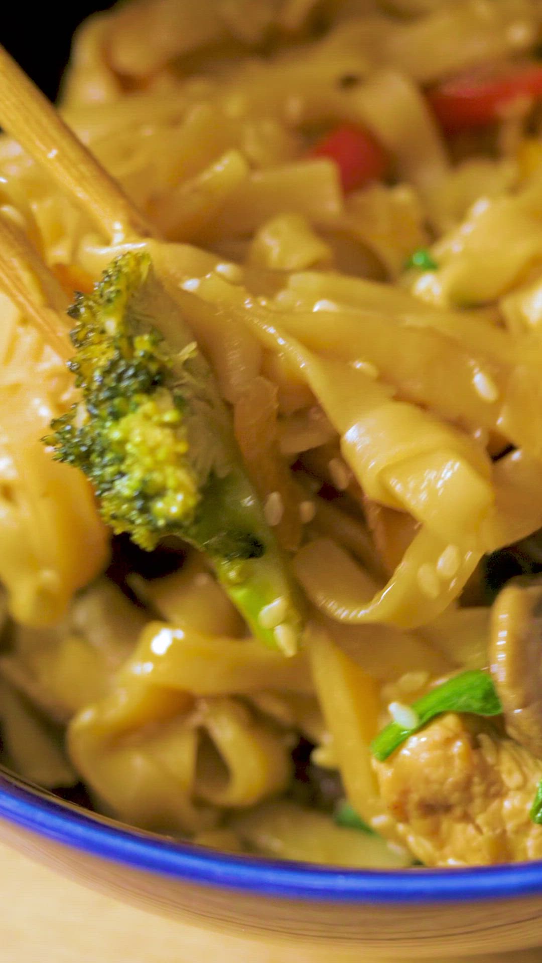 This may contain: a blue bowl filled with pasta and veggies on top of a wooden table