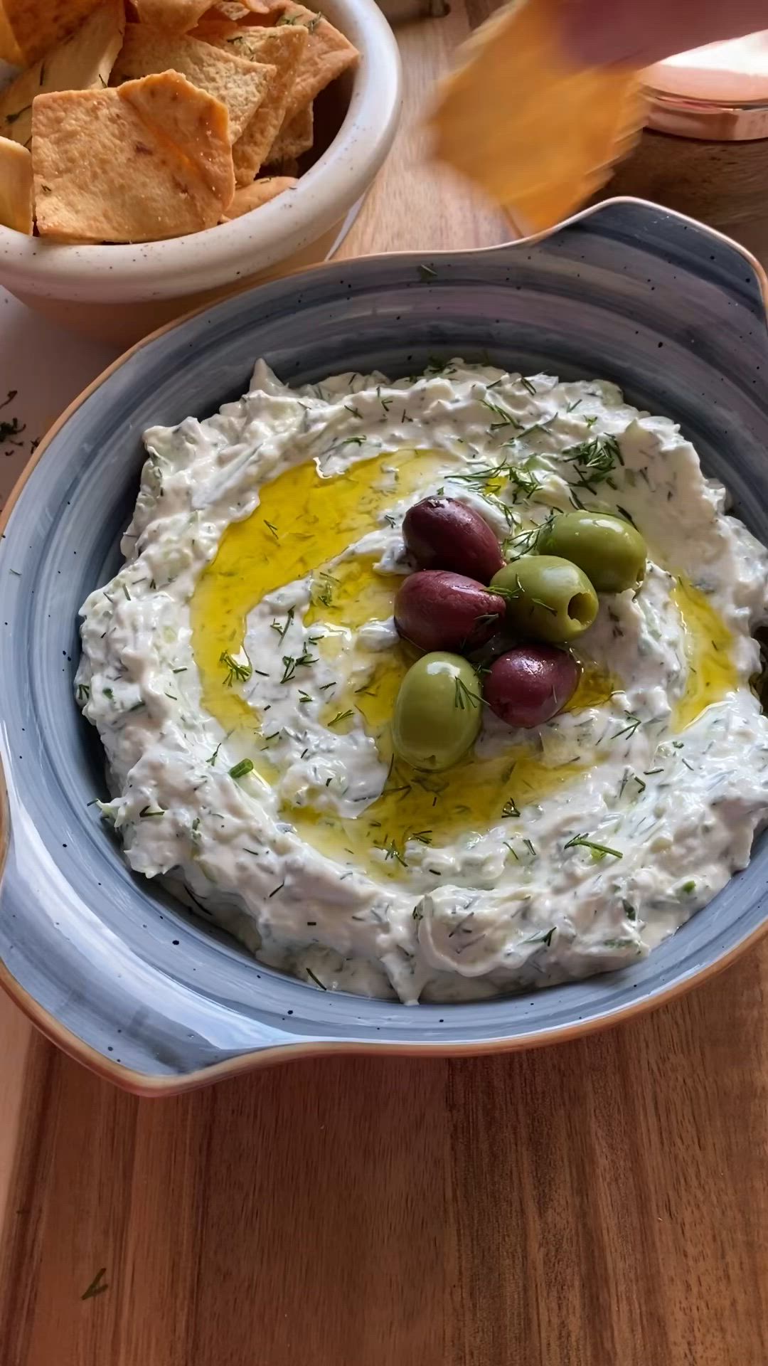 This may contain: a bowl filled with hummus and olives on top of a table next to chips