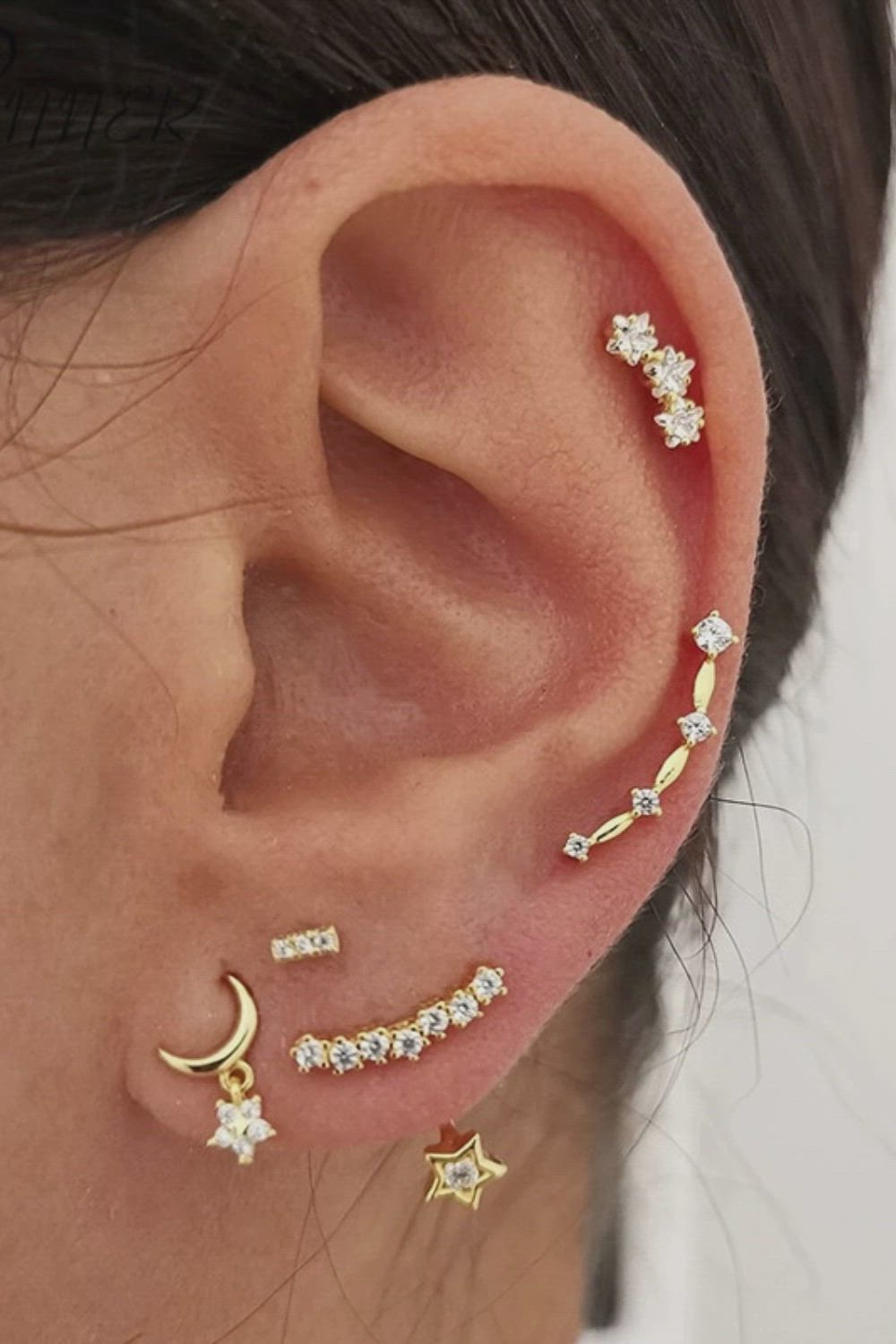 This may contain: a woman wearing three different ear piercings with stars, moon and crescent designs on them