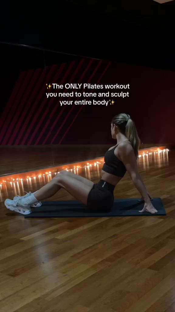 This may contain: a woman is sitting on a yoga mat in the middle of a room with lights behind her