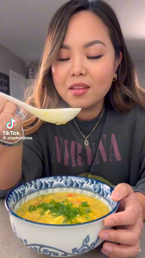 This may contain: a woman is eating soup from a blue and white bowl