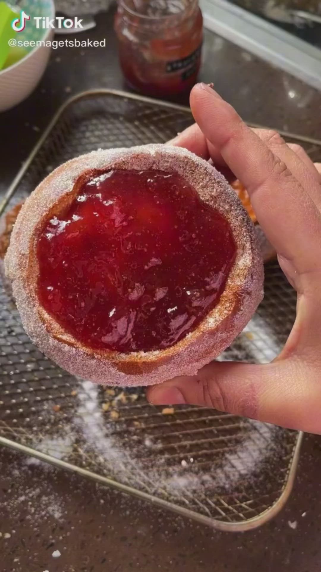 This may contain: someone holding up a jelly filled doughnut in front of some other food on a cooling rack