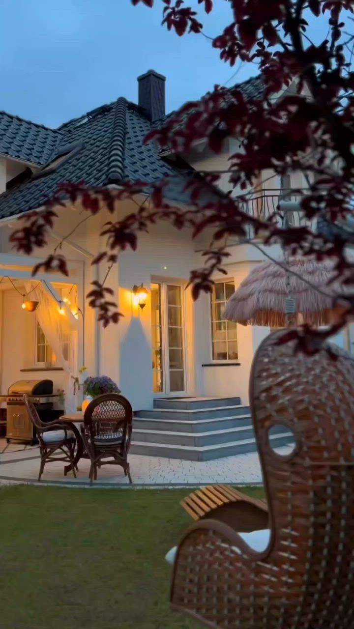 This may contain: an outdoor dining area with wicker chairs and umbrellas in front of a white house