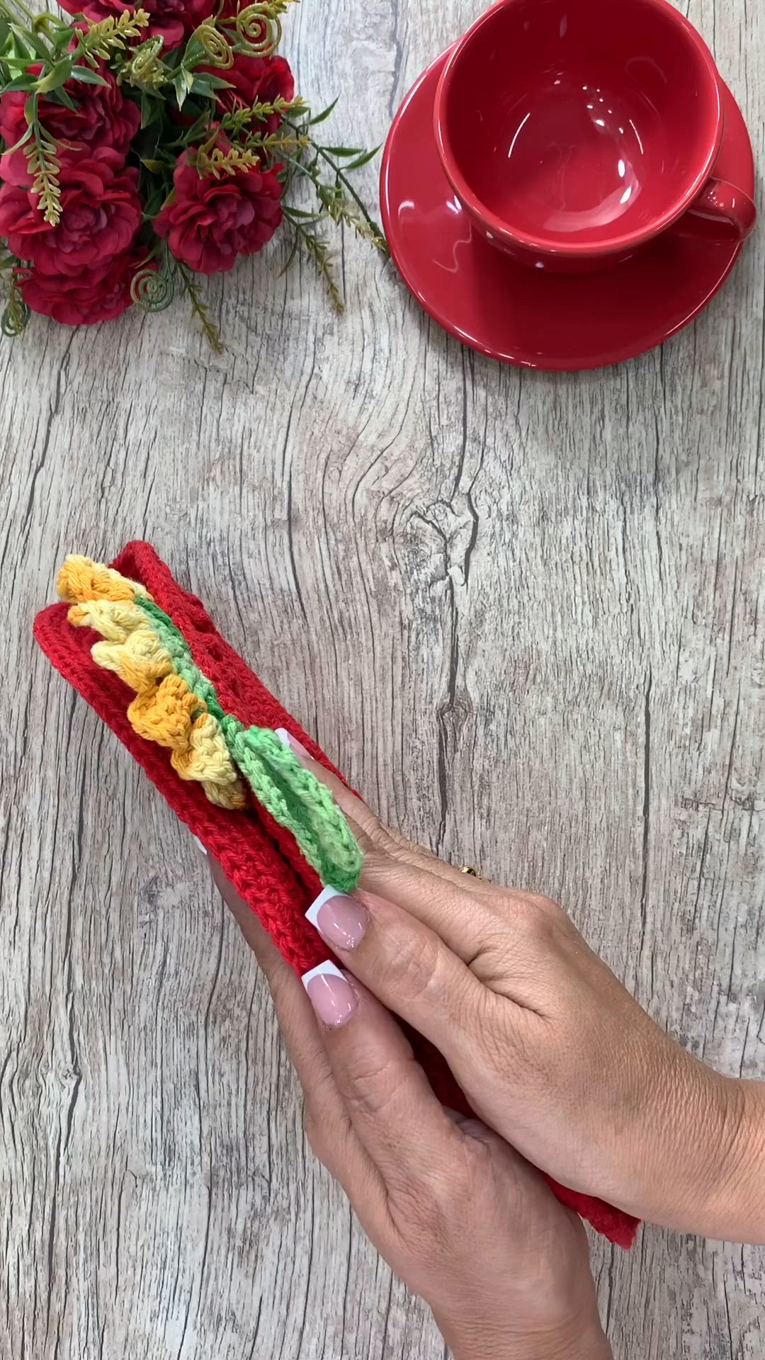 This may contain: a person holding a crocheted object on top of a wooden table next to flowers