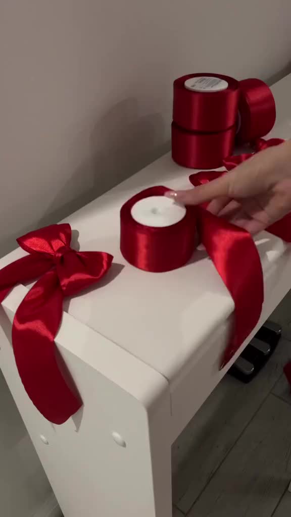 This may contain: a person is holding two rolls of red ribbon on top of a white table with some candles