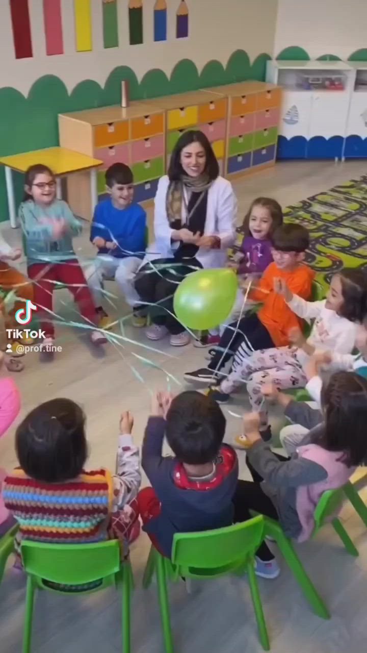 This may contain: a group of children sitting around each other in front of a woman holding a green balloon