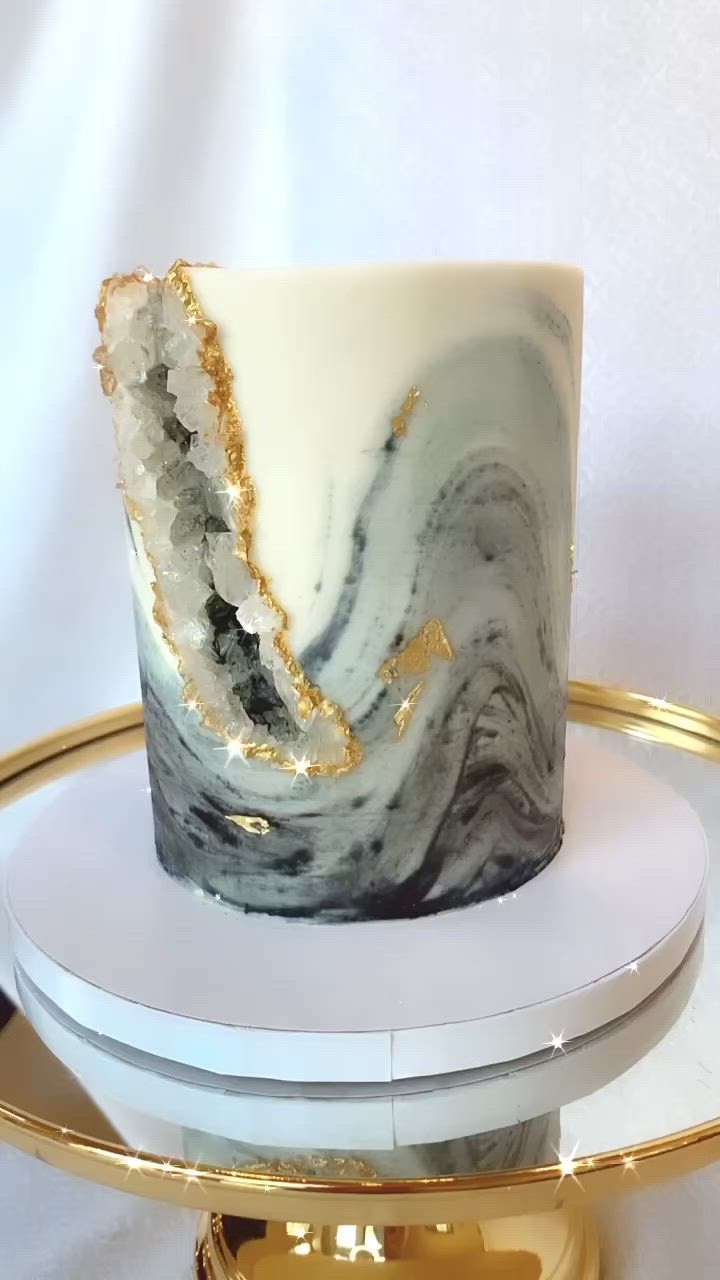 This may contain: a marble cake sitting on top of a gold plate with a white and black frosting