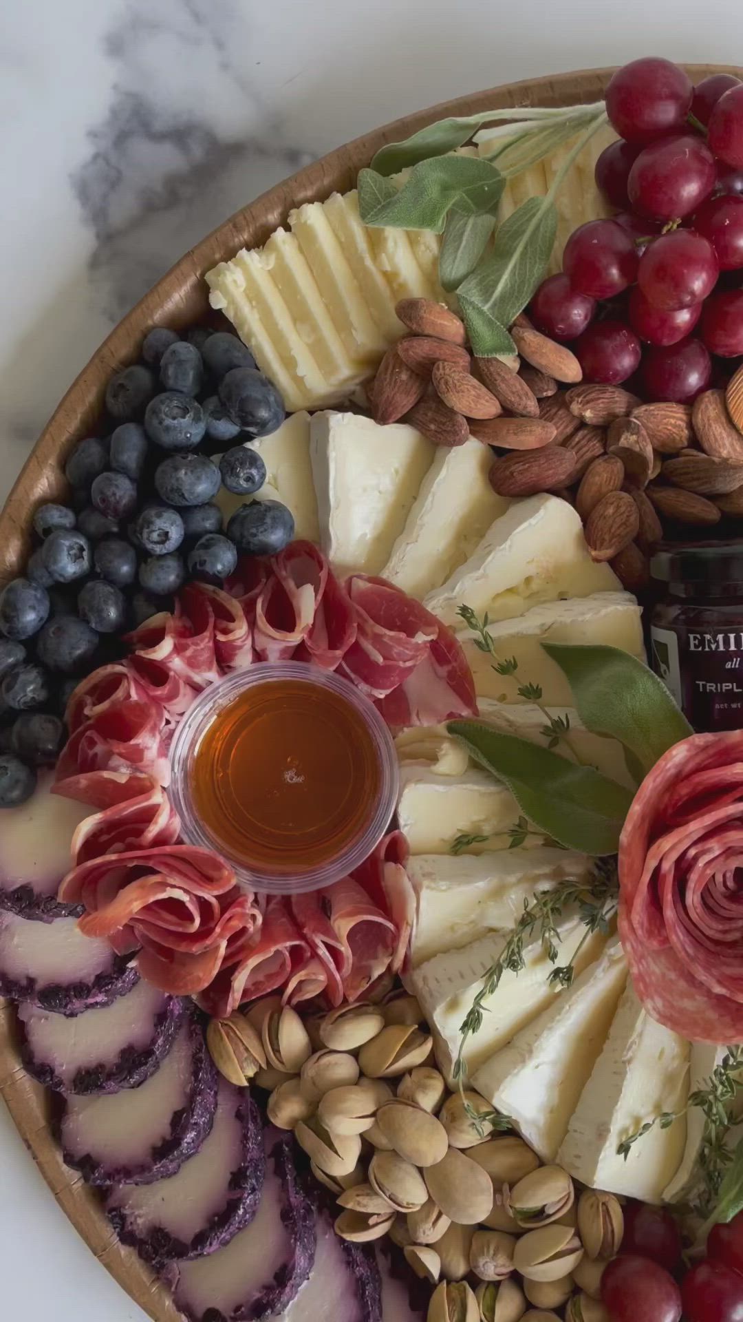 This may contain: a platter filled with cheese, grapes, nuts and other foods on top of a marble counter