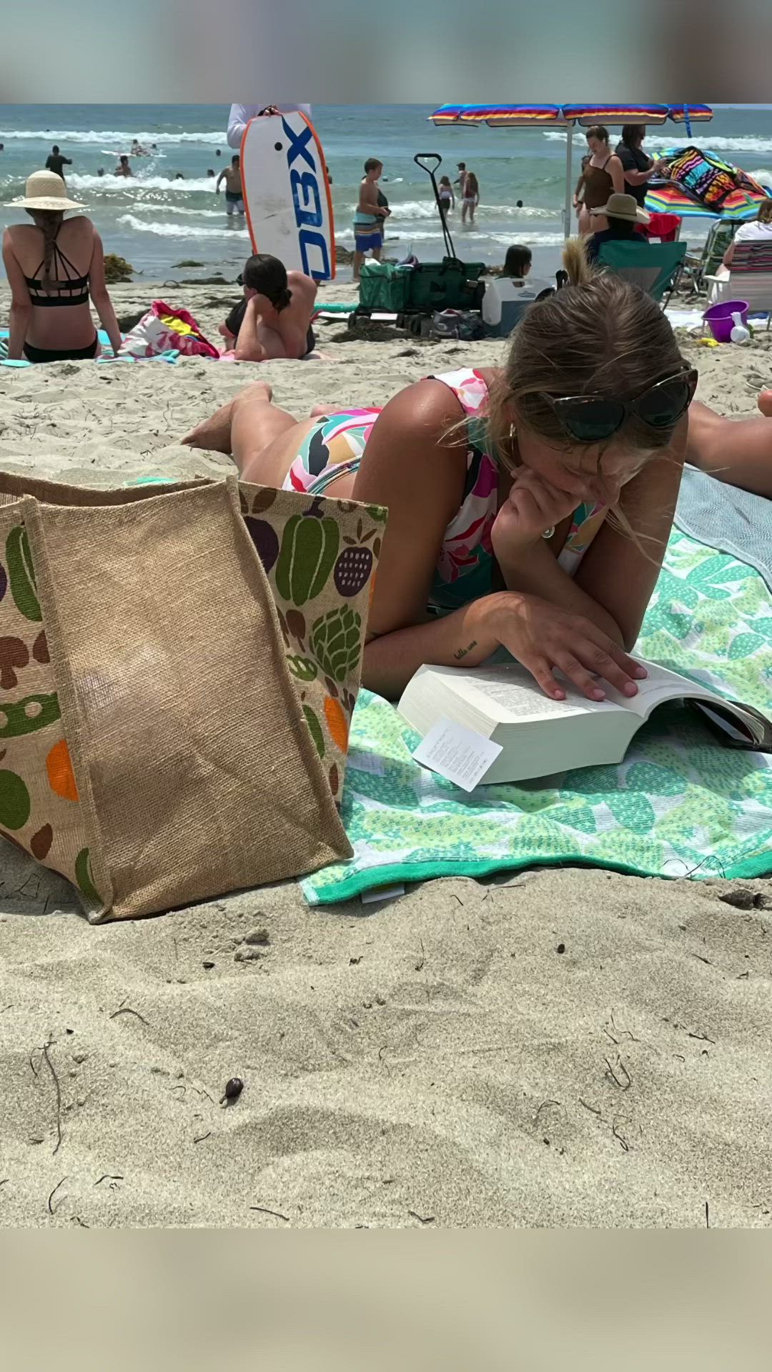 This may contain: a woman laying on the beach reading a book