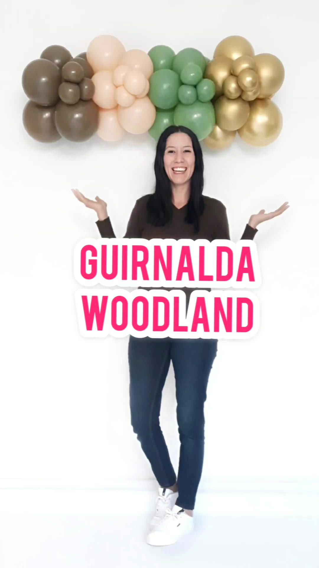 This may contain: a woman holding a sign that says gurnaldda woodland in front of balloons