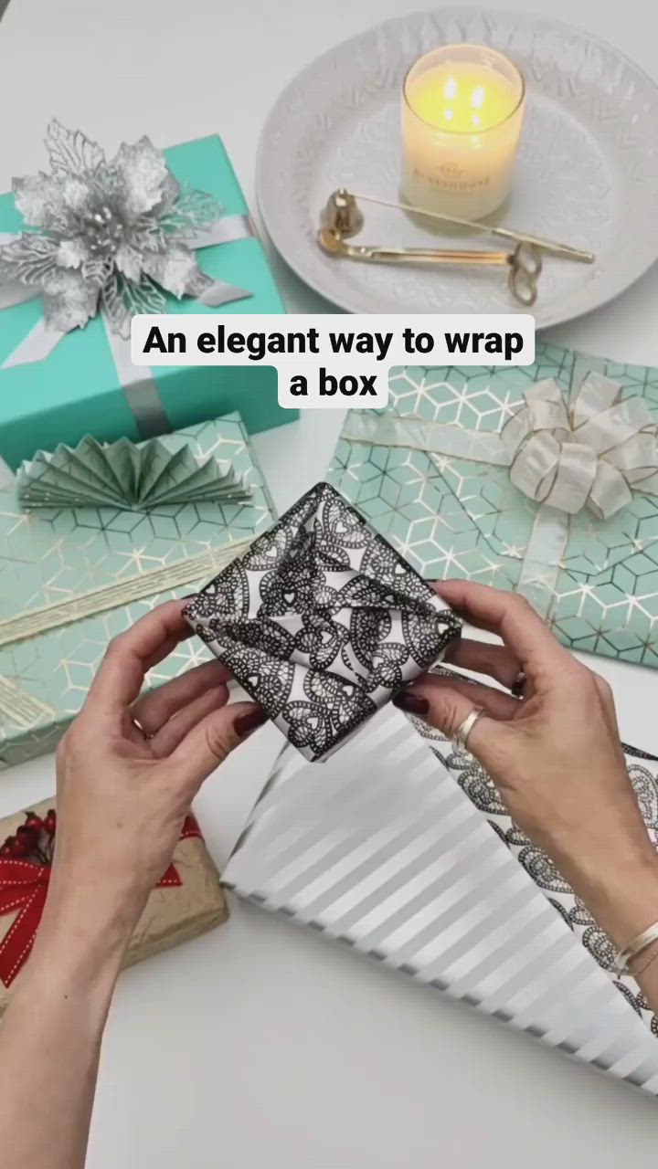 This may contain: someone is wrapping presents on a table with candles and other items in the background that reads, an elegant way to wrap a box