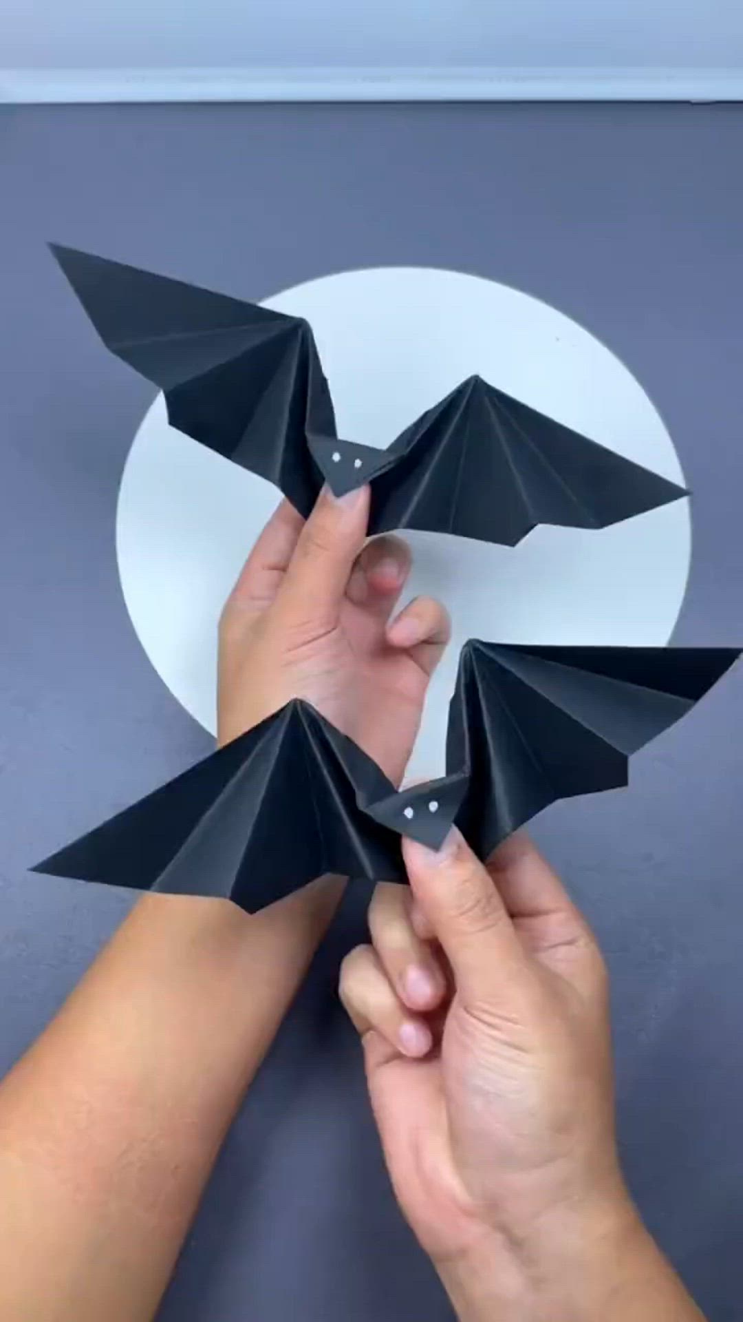 This may contain: two hands are holding black origami bats on a white circular surface with a gray circle in the background