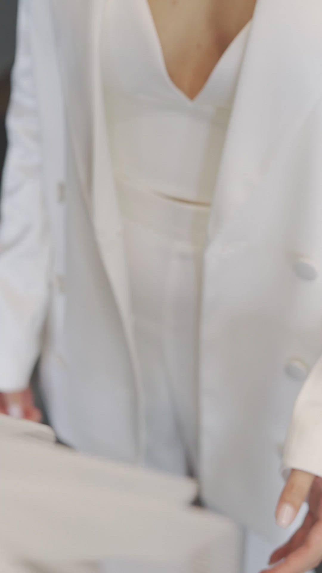 This may contain: a woman in a white dress and jacket cutting a piece of cake with a knife