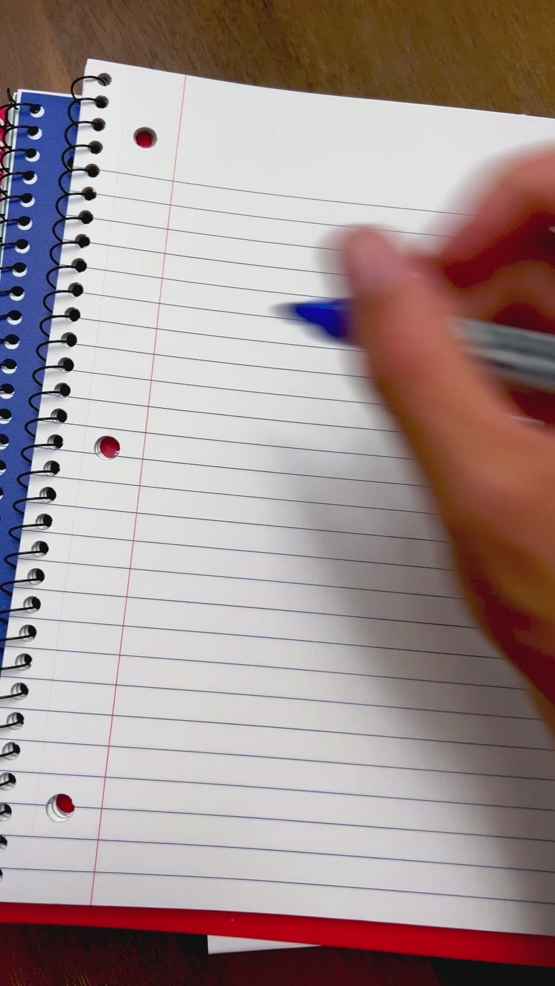 This may contain: a person writing on lined paper with a blue pen in their left hand and red dotted notebook next to them