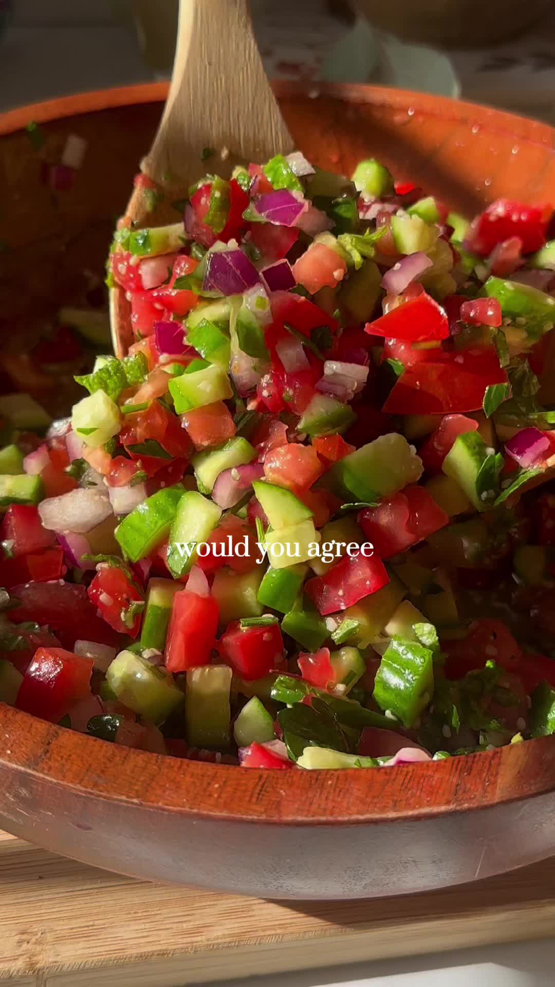 This may contain: a wooden bowl filled with cucumber and tomato salad next to a wooden spoon