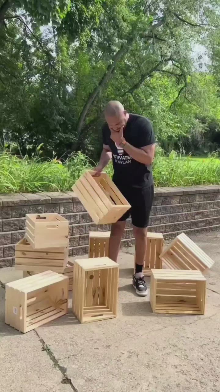 This may contain: a man standing next to stacks of wooden crates in front of a brick wall and trees