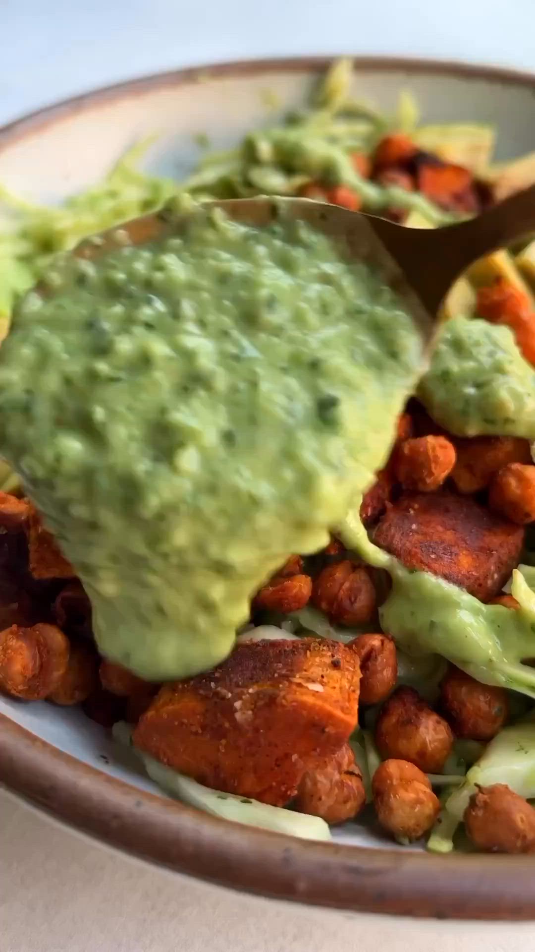 This may contain: a white plate topped with lettuce and chickpeas covered in guacamole