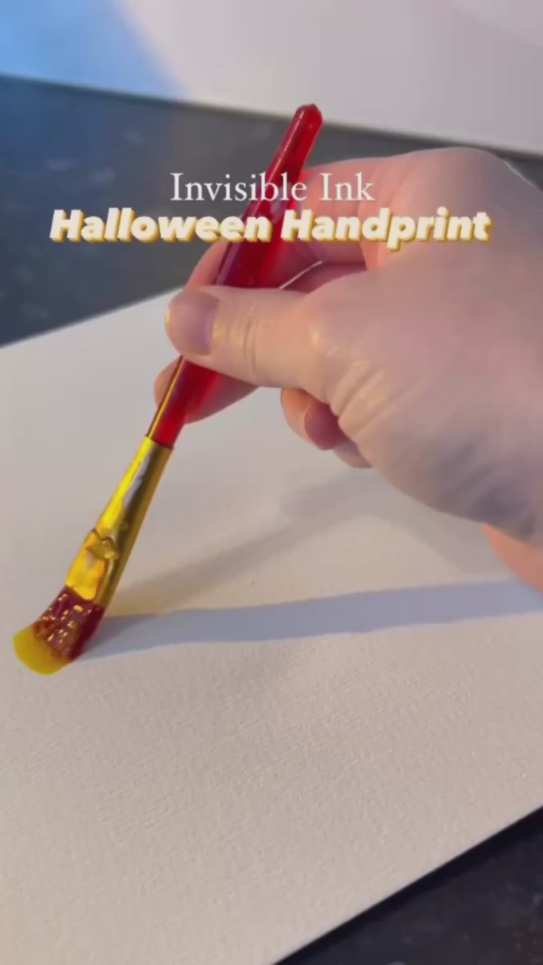 This may contain: a person holding a paintbrush over a piece of paper with yellow and red designs on it