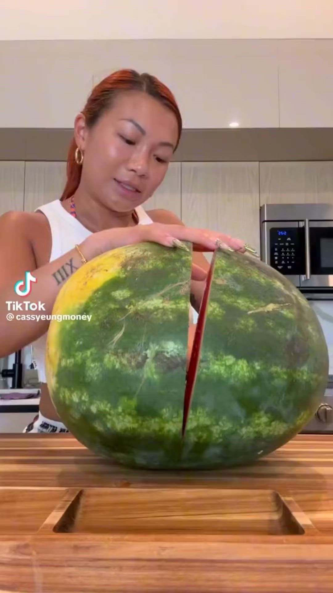 This may contain: a woman cutting up a large watermelon in the kitchen