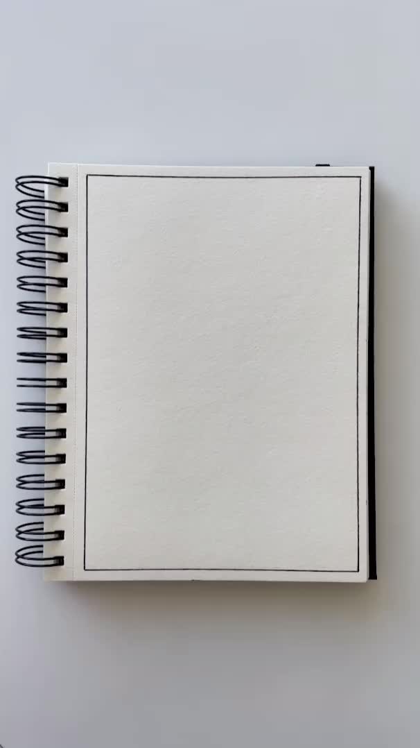 This may contain: a spiral notebook with black and white lines on the cover, sitting on top of a table