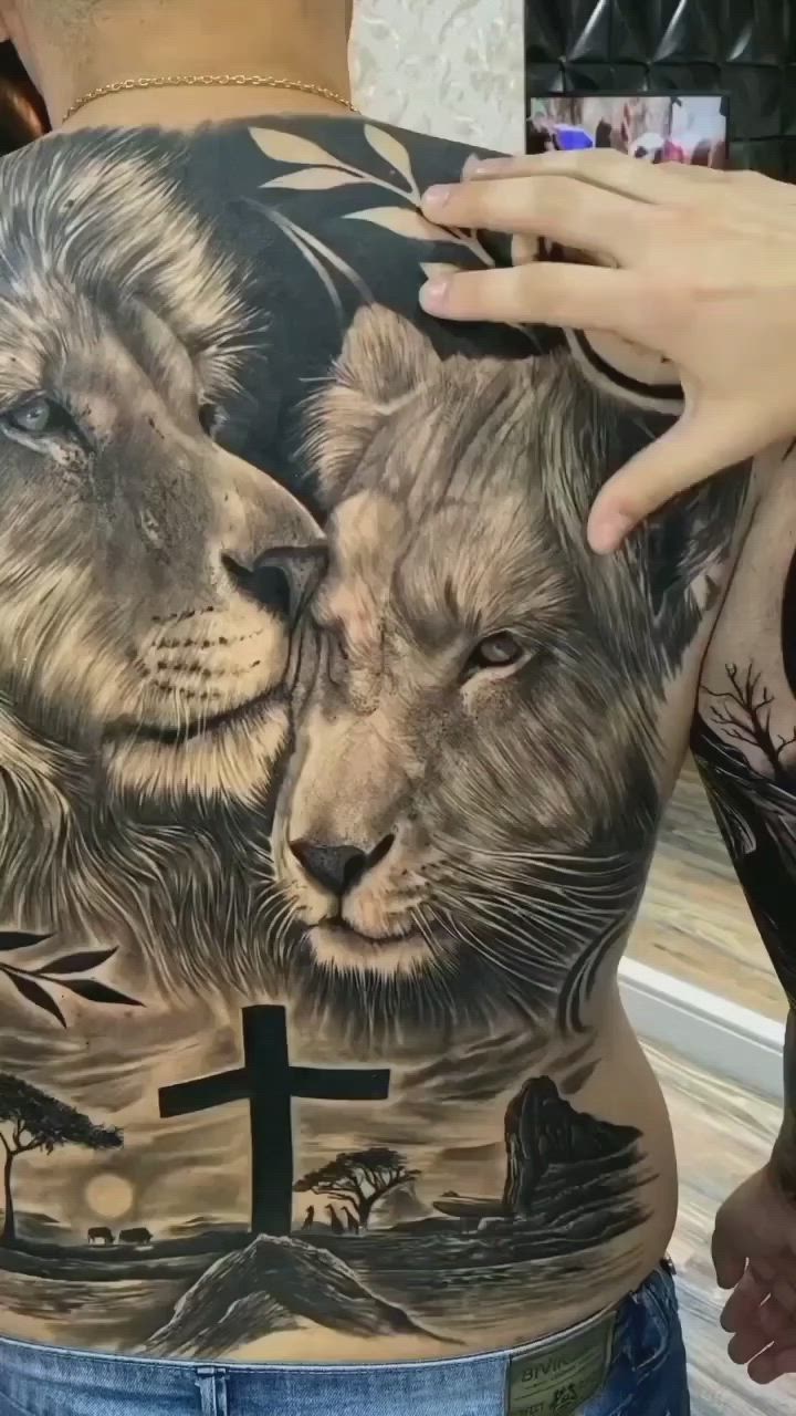 This may contain: a man with a lion tattoo on his back and cross in the other hand,